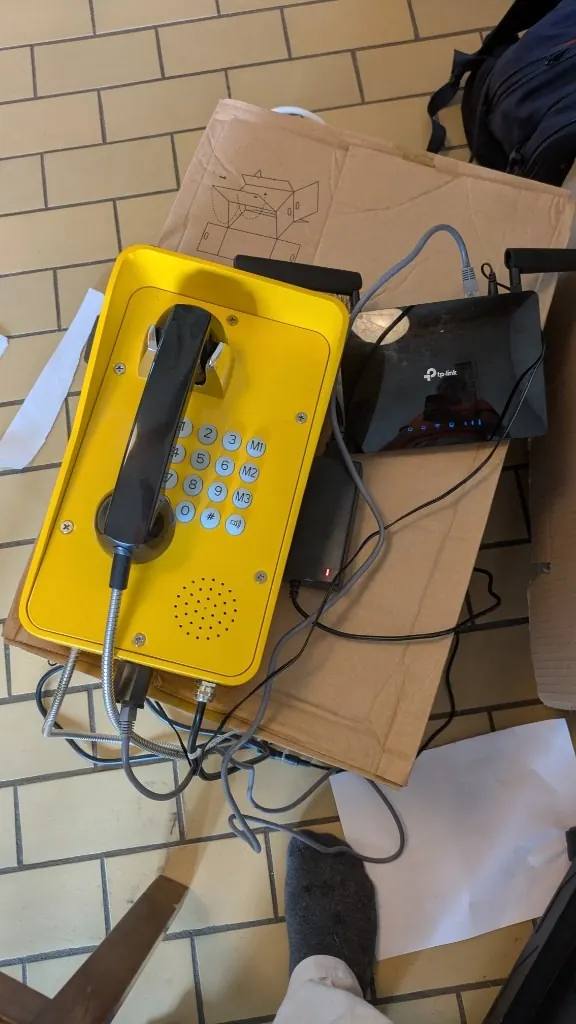The yellow phone and a 4G router on a cardboard box on a workbench, in daylight