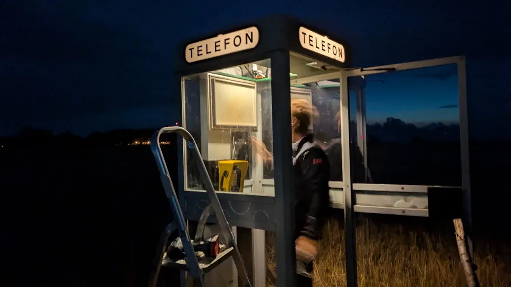 Working in the booth at dusk with a ladder, the yellow phone visible inside